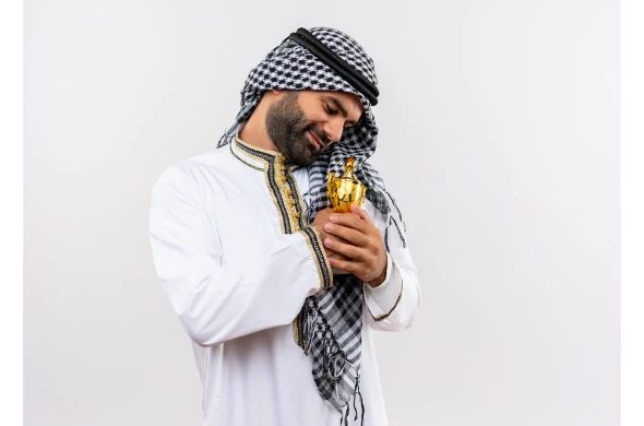 hombre-arabe-en-ropa-tradicional-abrazando-su-trofeo-sonriendo-sintiendo-emociones-positivas-de-pie-sobre-la-pared-blanca