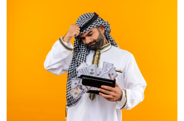 hombre-de-negocios-arabe-en-ropa-tradicional-sosteniendo-la-billetera-con-dinero-en-efectivo-que-parece-confundido-y-muy-ansioso-de-pie-sobre-la-pared-naranja